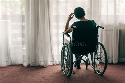 Печальная грустная женщина в изношенной инвалидной коляске глядя в окно Стоковое Фото