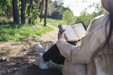 christian woman holds bible in her hands reading the holy bible in a field during beautiful