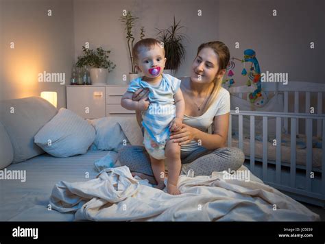 Young Mother Changing Messy Diapers To Her Baby Boy On Bed At Night