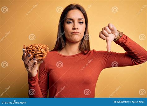 Young Beautiful Brunette Woman Holding Bowl With Germany Baked Pretzels With Angry Face