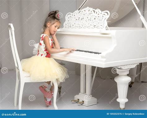 Beautiful Little Girl Is Playing On A White Grand Piano Stock Photo