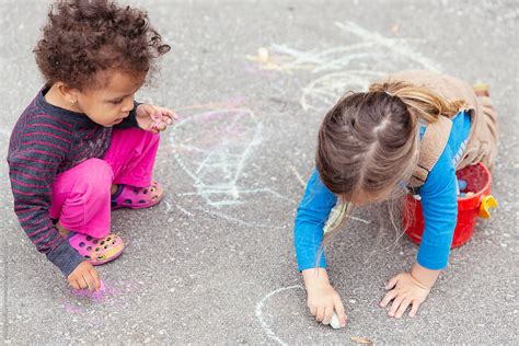 Kids Drawing In The Driveway With Large Pieces Of Chalk By Stocksy