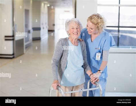 Nurse Helping Senior Patient With Walker In Hospital Corridor Stock