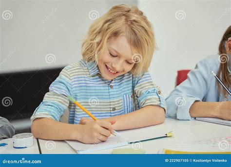 Joyful Little Schoolboy Smiling Holding Pencil And Making Notes While