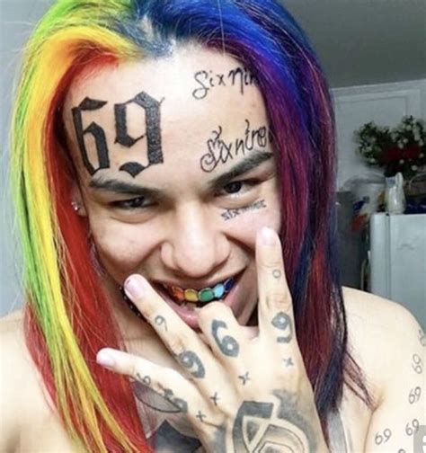 A Man With Multicolored Hair And Tattoos Holding His Hand Up To His Face