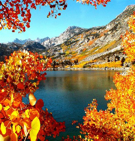 A Lake Surrounded By Mountains And Trees With Orange Leaves In The