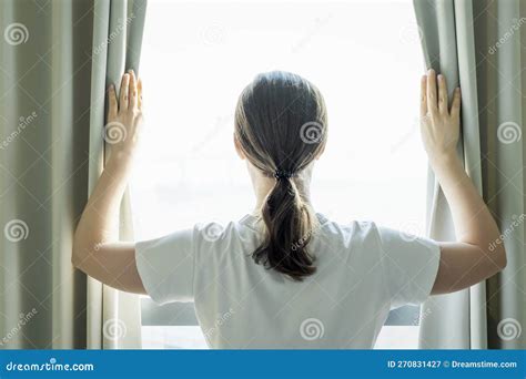 Young Woman Stands At Window And Opens Curtains Back View Stock Image