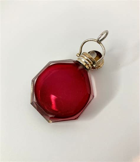 A Red Glass Bottle Is Sitting On A White Surface And Has A Gold Chain Around It
