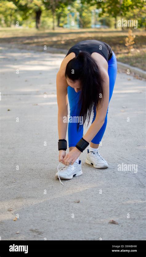 Woman Athlete In Sportswear Bending Down And Tying Her Shoelaces On Her