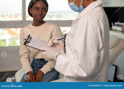 Smiling Female Patient Asking Questions Of Doctor In Clinic Stock Photo