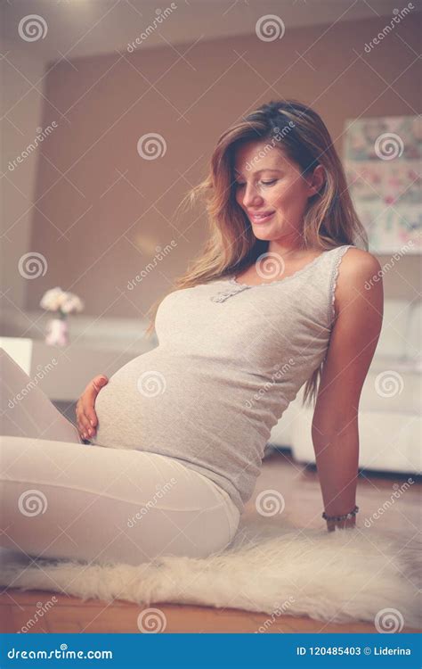 Pregnant Brunette Woman Touching Her Belly And Sitting On Floor Stock