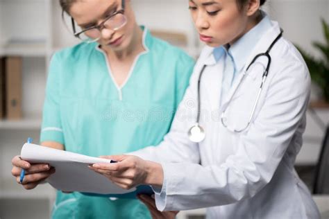 Doctors Looking At Clipboard Together At Clinic Stock Image Image Of