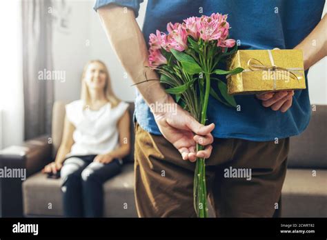 Husband Hiding Romantic Surprise Present And Flowers Behind Back To Beloved Wife At Home Stock