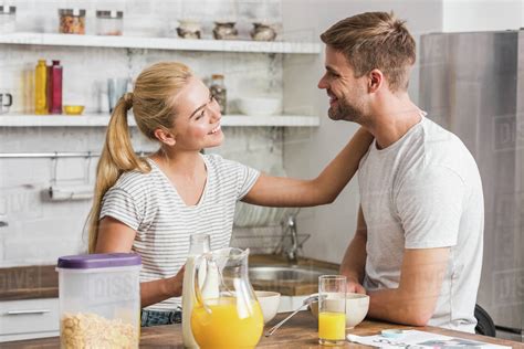 smiling girlfriend touching boyfriend during breakfast in kitchen ...