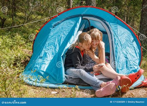 Girls Using Smartphone Sitting In A Camping Tent During Summer Holidays
