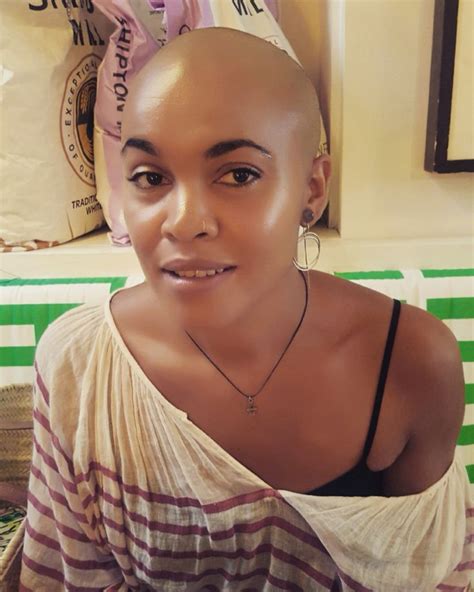 A Woman With A Shaved Head Sitting In Front Of A Table And Looking At The Camera