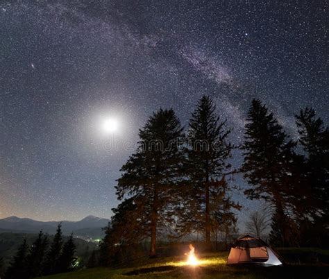 Night Camping In Mountains Tourist Tent By Campfire Near Trees Under