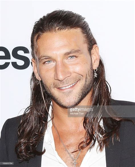 A Man With Long Hair Wearing A Black Suit And White Shirt Smiles At The Camera