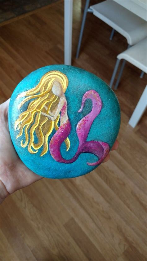 A Hand Holding A Painted Rock With A Mermaid On It