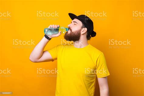Photo Of Young Bearded Man Drinking Water Over Yellow Background Stock