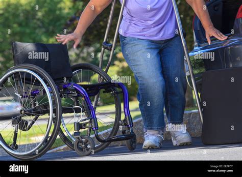 Woman With Spina Bifida About To Sit In Wheelchair After Putting It Together Outside Car Stock