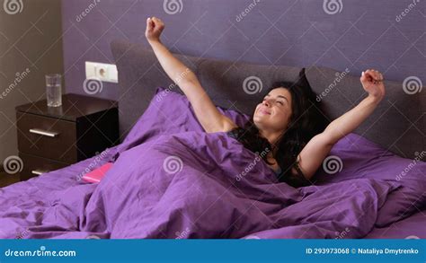 Attractive Young Woman Waking Up In Bed In The Morning Yawning While Stretching Arms At Bedroom