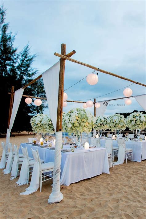 An Outdoor Wedding Set Up On The Beach With White Linens And Flower