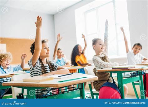 Group Of Schoolchildren Raising Hands To Answer Question Stock Photo
