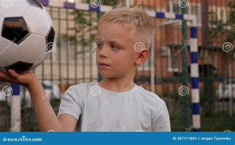 A Little Boy Holds A Soccer Ball On The Football Field In The Courtyard