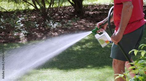 Man Fertilizing Residential Backyard Lawn With Liquid Chemical Spreader