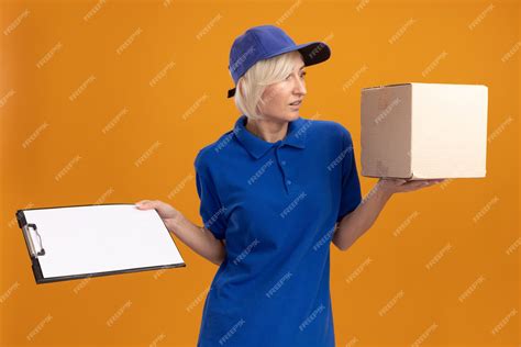 Free Photo Impressed Middle Aged Blonde Delivery Woman In Blue Uniform And Cap Holding Cardbox