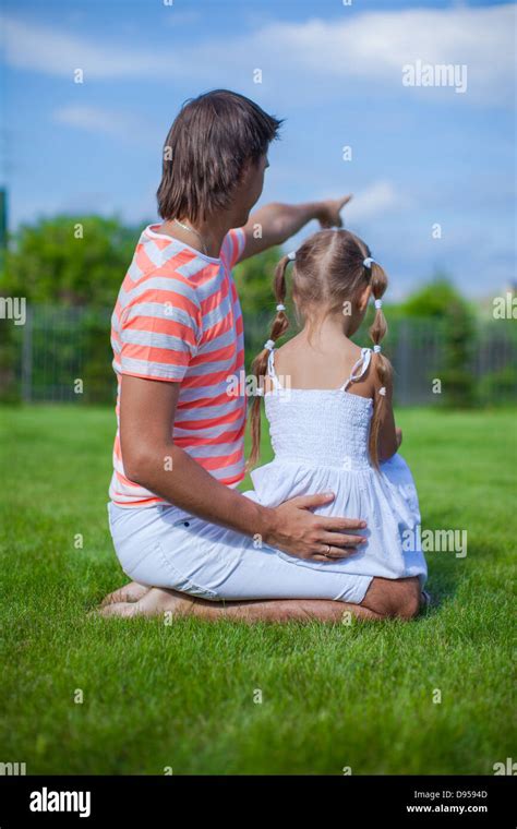 Back View Of Father With His Daughter Sitting In The Yard Outdoors
