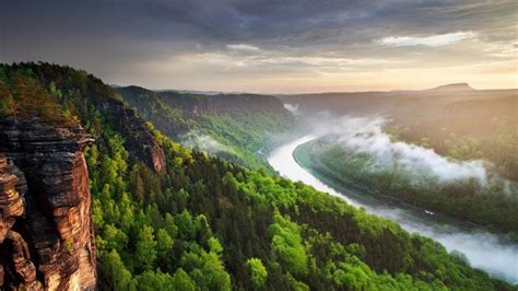 Aerial View Of River Between Foggy Green Trees Forest Rock Mountains