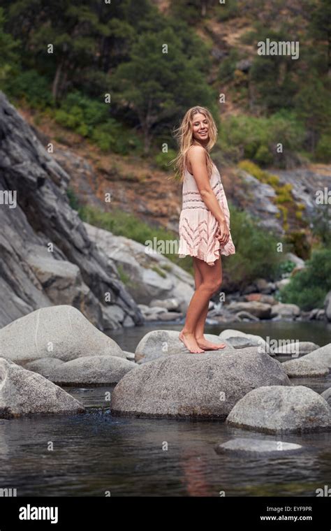 A Young Barefoot Woman In A Summer Dress Standing On A Rock In A