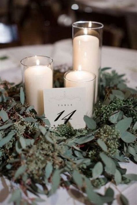 Two Candles Sitting On Top Of A Table Covered In Greenery And Leaves