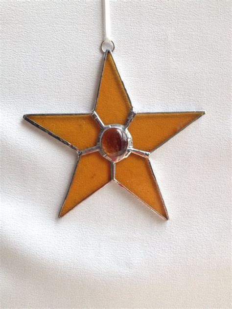 A Stained Glass Star Ornament Hanging On A White Cloth With A Red Bead