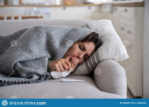 Sick Unhealthy Woman Lying Under Blanket On Sofa Coughing And Sneezing