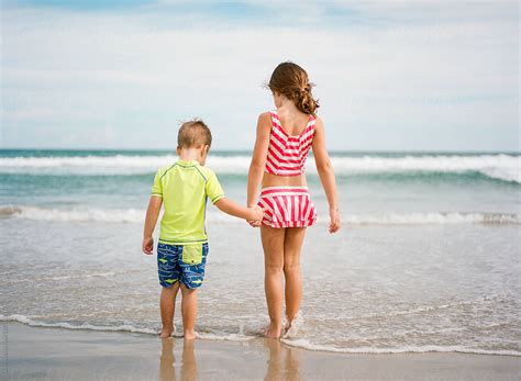 Big Sister Holding Little Brothers Hand While Walking Towards The Ocean Stocksy United