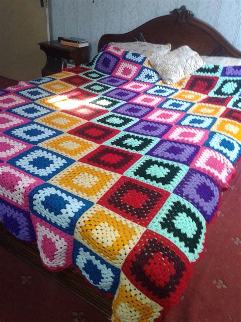 A Crocheted Granny Blanket On Top Of A Bed In A Room With A Wooden