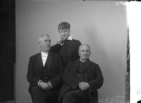 gruppbild med två sittande äldre män en kvinna står bakom dem lutad mot den ena en av männen