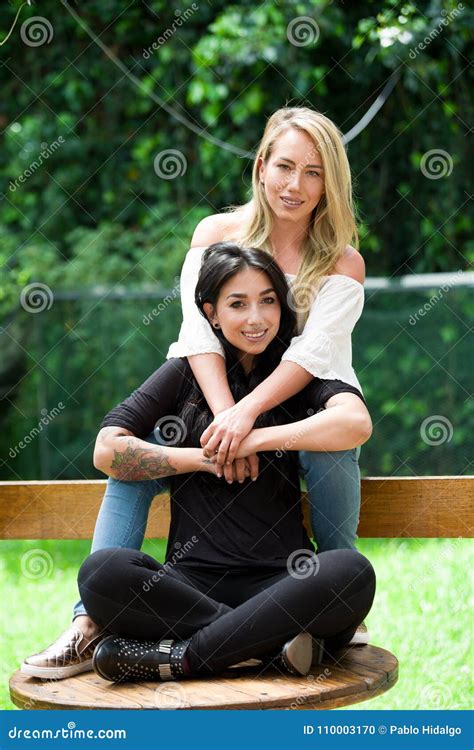 a pair of proud lesbian sitting in outdoors looking at each other and go kissing in a garden