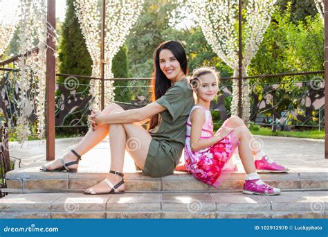 Attractive Mom And Daughter Sitting On Stairs In Beautiful Park Stock