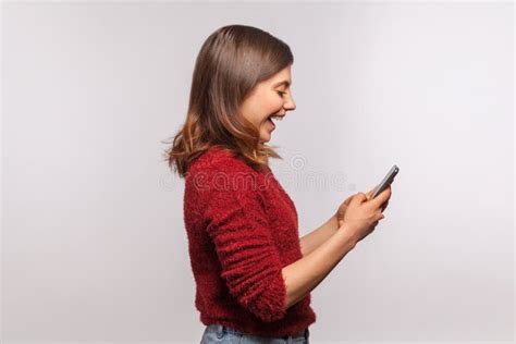 side view amazed brunette girl in shaggy sweater using mobile phone with surprised expression