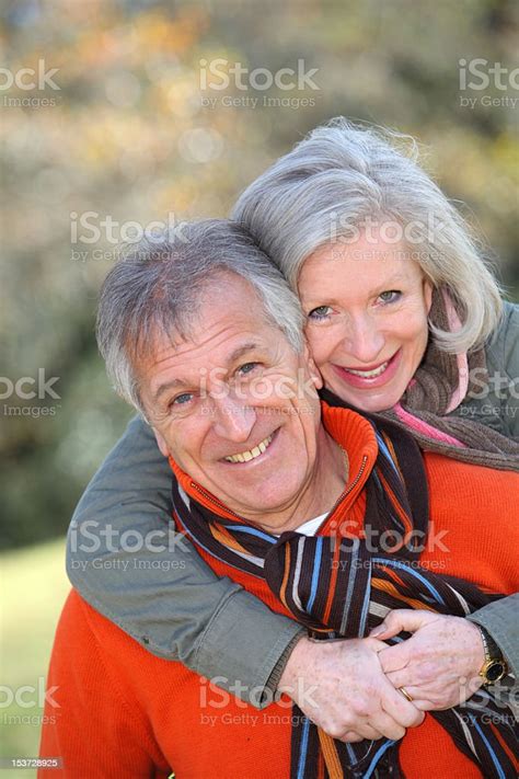 A Smiling Senior Woman Hugs Her Husband From Behind Stock Photo