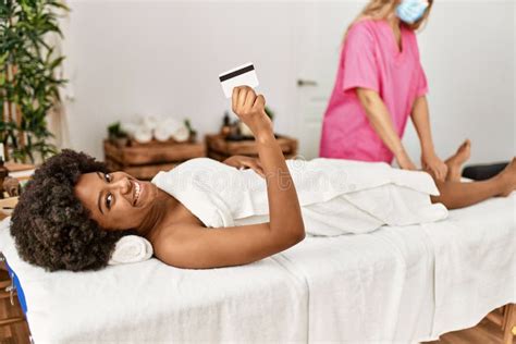 Young African American Woman Holding Credit Card Having Legs Massage At Beauty Center Stock