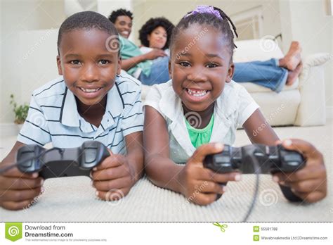 Happy Siblings Lying On The Floor Playing Video Games Stock Photo