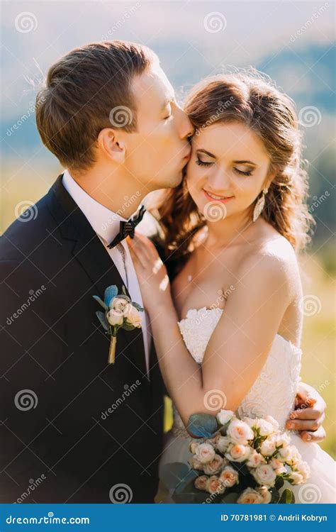 Loving Groom Kissing Bride S Forehead On The Meadow With Mountain