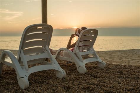 Dusk On A Beach At Sunset As A Woman Relaxes On A Recliner Chair Stock