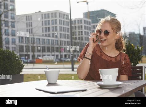 Young Woman Talking On A Mobile Phone At Sidewalk Cafe Munich Bavaria