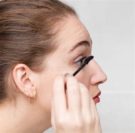 Closeup Profile Of Young Woman Applying Mascara On Her Eyelashes Stock